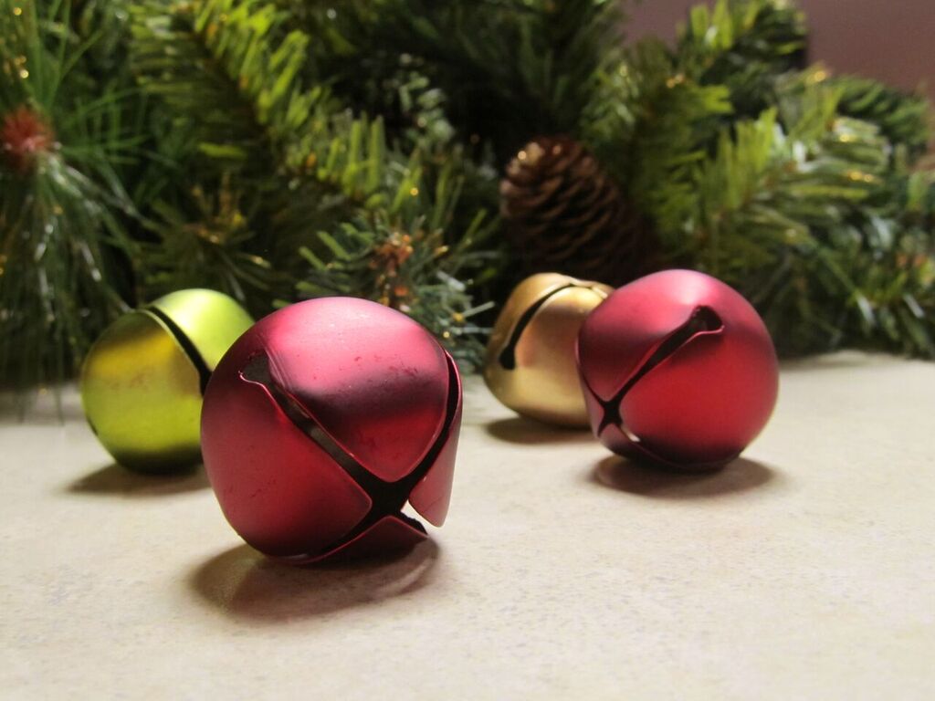 close up of red and green sleigh bells with pine tree branches in background